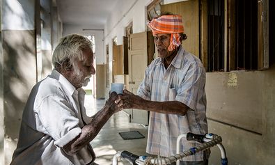 Das Leprosy Relief Rural Center in Chettipatty, Indien. Cheety, 80, Leprapatient benutzt die Klinik als Referenzzentrum. Nachdem er mit seinem Walker eine halbe Stunde zur Klinik gelaufen ist bringt ihm Perumal Wasser  zum Trinken.