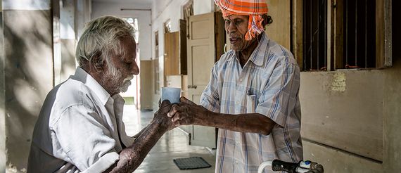 Das Leprosy Relief Rural Center in Chettipatty, Indien. Cheety, 80, Leprapatient benutzt die Klinik als Referenzzentrum. Nachdem er mit seinem Walker eine halbe Stunde zur Klinik gelaufen ist bringt ihm Perumal Wasser  zum Trinken.