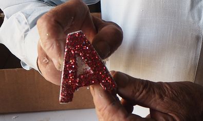 Ein Heimbewohner fertigt glitzernde Buchstaben an und verdient sich so seinen Lebensunterhalt.